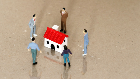 Five miniature people staring down a house of red roof miniature.の写真素材