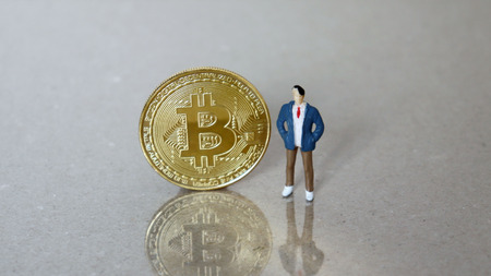 A miniature man standing next to the bitcoin.の写真素材