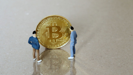 Two miniature men standing in front of a Bitcoin.の写真素材