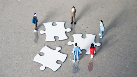 Five miniature people staring down three pieces of the puzzle.の写真素材