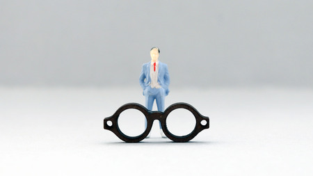 The concept of social prejudice against men. A miniature man in a suit standing behind glasses.の写真素材