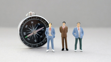Three miniature men standing in front of the compass.の写真素材