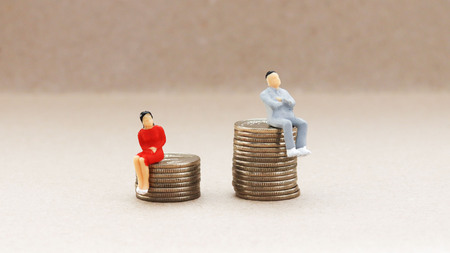 Gender discrimination concept. A miniature woman and a man sitting on a pile of coins.の写真素材