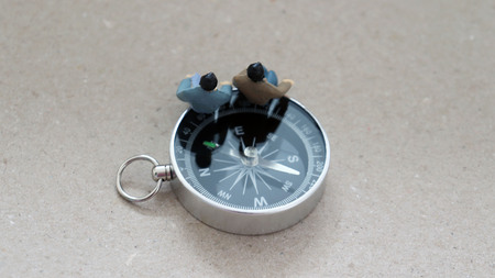 Appearance from behind two miniature men sitting on a compass.の写真素材
