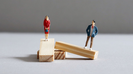 A miniature man and a miniature woman standing on a twisted block of wood.の写真素材