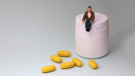 A miniature man sitting on a medicine bottle.の写真素材