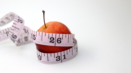 A red apple with a tape measure on a soft white background.
