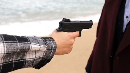 A hand pointing a gun at a woman in a coat.の写真素材