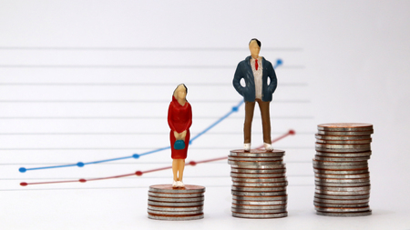 A miniature man and a miniature woman standing on a pile of coins with a flow linear graph. The concept of the wage gap between men and women in the workplace.の写真素材