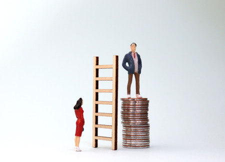 A pile of coins and miniature people. Differentiated treatment concepts for men and women at work.の写真素材