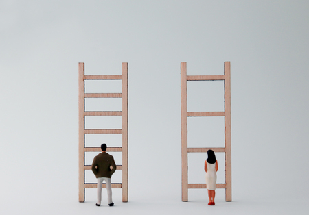 Miniature men and women standing in front of different ladders. A gender discriminatory concept of employment.の写真素材