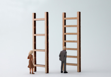 Miniature men and women standing in front of different ladders. The standard concepts are discriminatory against men and women in their work.の写真素材