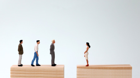 A miniature man and a woman standing on a block of wood. Gender inequality concepts in employment and promotion.の写真素材