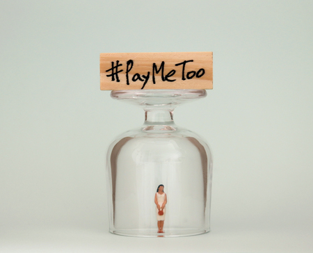 #PayMeToo as a new social movement. A miniature woman in a glass cup and a wooden block with #PayMeToo written on top of a glass cup.の写真素材