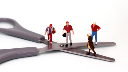 Two miniature men and women standing on top of a pair of scissors. The concept of the income gap between individuals.の写真素材