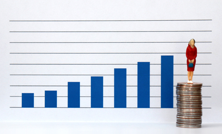 A miniature people standing on a pile of coins and a blue bar graph against the white background.の写真素材