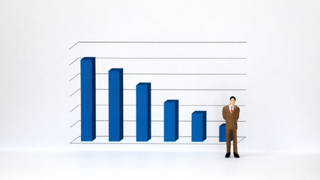 A miniature man in a suit standing in front of a three dimensional bar graph.の写真素材