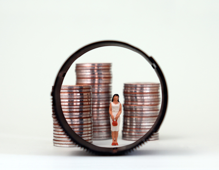 A miniature woman standing between three piles of coins. The changing concept of women and social conflict in modern times.の写真素材