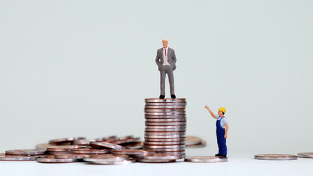An economic gap concept. A pile of coins and miniature people.の写真素材