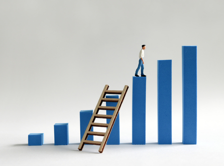 A miniature man walking across a bar of blue bar graph with a ladder across. The desire for promotion and success.の写真素材