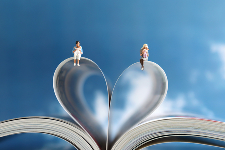Miniature people sitting on the heart shape paper book against the blue sky. An absolute love concept for a mother's child.の写真素材