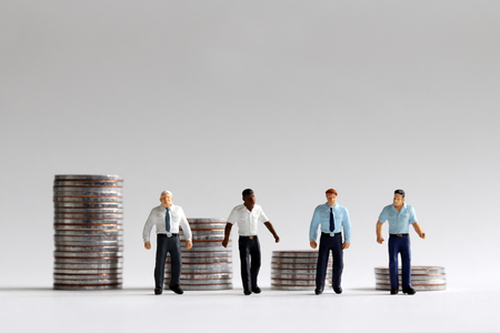 The concept of wage and labor disparity. A stack of four different coins and four miniature men.の写真素材