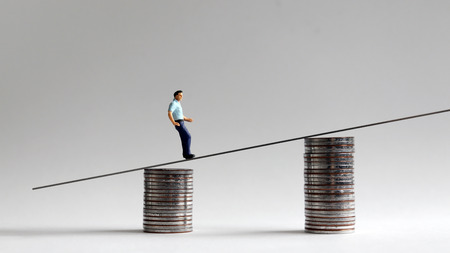 The concept of a gap between wages and inflation. Miniature people with two stacks of coins.の写真素材