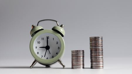 Two piles of coins that are different in height from the alarm clock.の写真素材