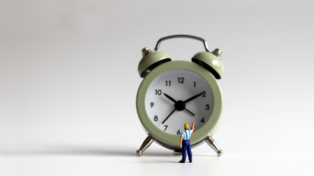 A miniature man pointing to an alarm clock.