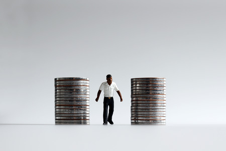 A miniature man walking between piles of coins.の写真素材