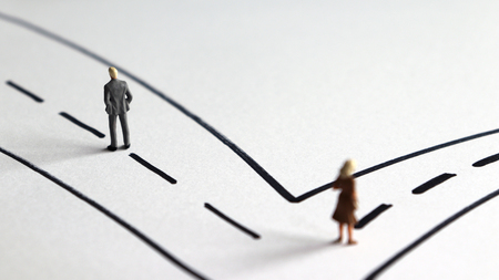 A miniature man and a miniature woman heading two different paths.の写真素材