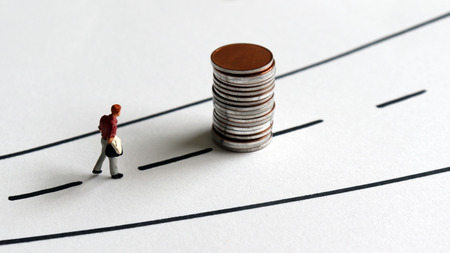 A miniature man walking to a pile of coins.の写真素材