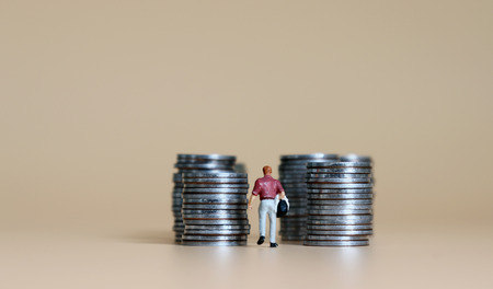 A concept of income. A miniature man walks among piles of coins.の写真素材