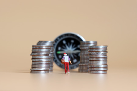A miniature woman walks among piles of coins and a compass.の写真素材