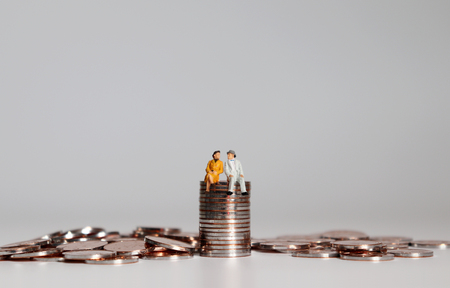 A pile of coins and miniature people. The concept is preparing for the expense of one's old age.の写真素材