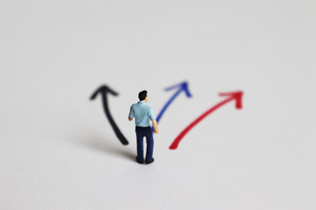 The back of a miniature man standing in front of three forked ways.