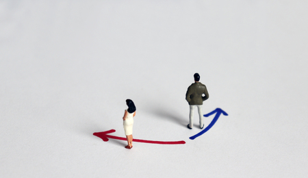 A miniature man standing in front of blue color direction with a miniature woman standing in front of red color direction.の写真素材