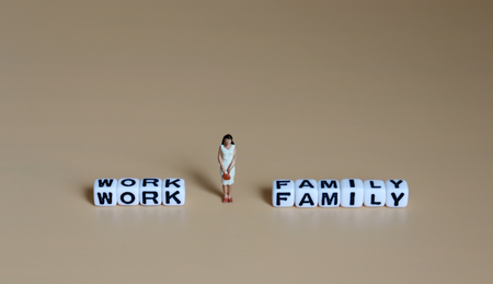 A miniature woman standing between a cube of 'WORK' and a cube of 'FAMILY' word.の写真素材