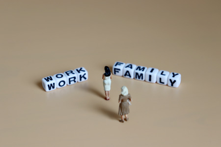 The back of two miniature women standing between a cube of 'WORK' and a cube of 'FAMILY' word.の写真素材