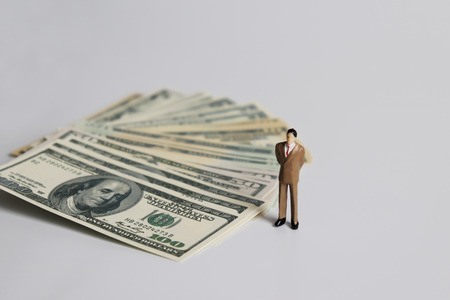 Miniature businessman standing next to the pile of dollars.