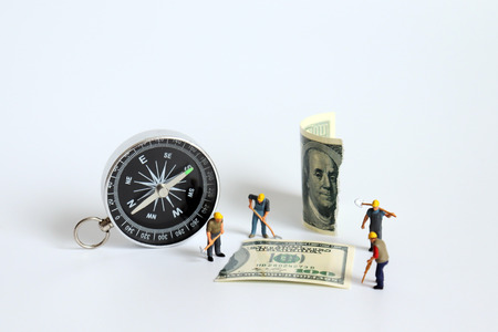 A compass next to a hundred dollar bill torn in half with a miniature worker.の写真素材