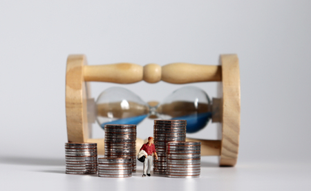 Miniature man with a sandglass and a pile of coins.