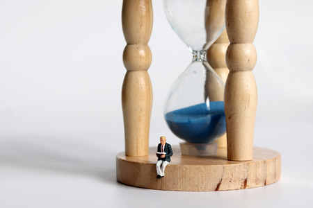 A miniature man sitting on a sandglass reading a book.の写真素材