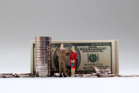 A miniature man and a miniature woman standing in front of a hundred dollar bill with a pile of coins.の写真素材