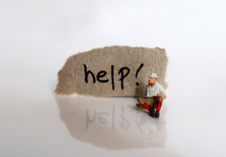 A miniature man sitting in front of a piece of paper. The 'help!' written on cardboard.の写真素材