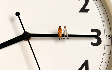 A miniature old couple sitting on a clock's needle.の写真素材