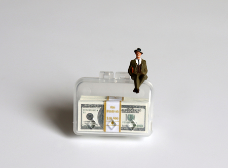 A miniature businessman sitting on a bag with a hundred-dollar bills.の写真素材