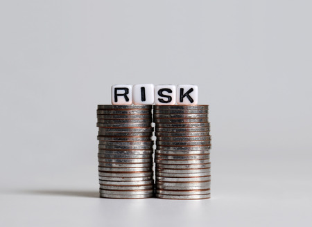 'RISK' text white cube on two pile of coins.