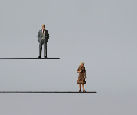 A miniature man and a miniature woman standing at different heights. The concept of discrimination in employment by gender.の写真素材
