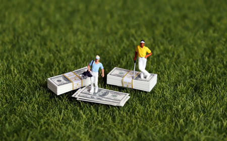 A bundle of bills and two miniature golfers on the green grass.
